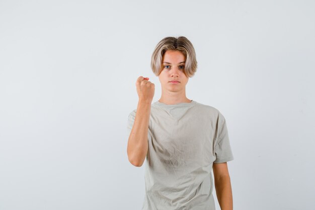 Jovem rapaz adolescente em t-shirt mostrando o punho cerrado e olhando sério, vista frontal.