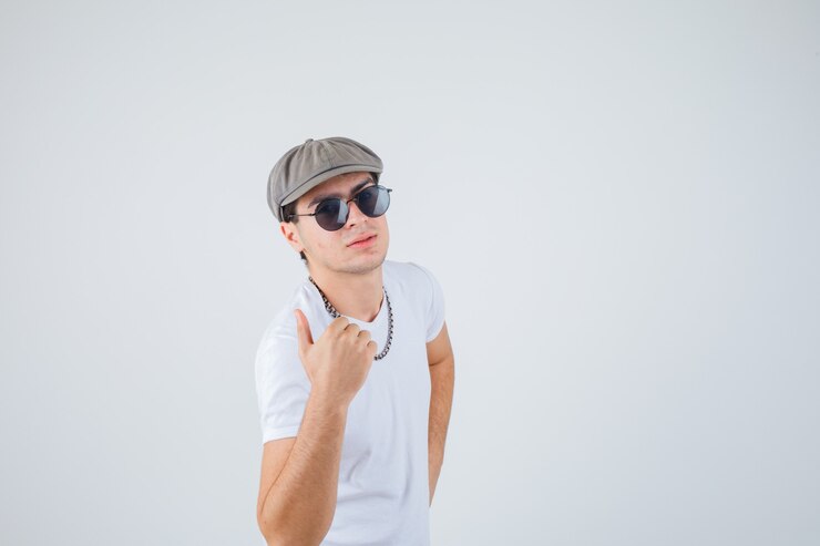 Foto grátis jovem rapaz aparecendo o polegar em t-shirt, chapéu e parecendo satisfeito. vista frontal.