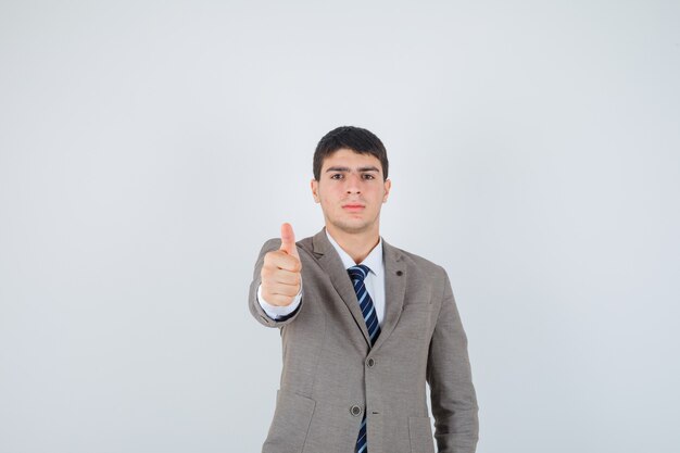 Jovem rapaz aparecendo o polegar em um terno formal e olhando confiante, vista frontal.