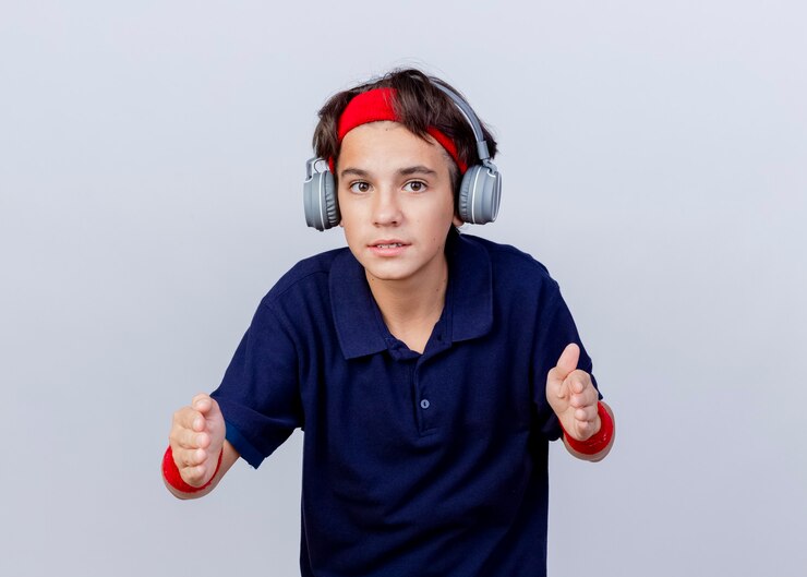 Foto grátis jovem rapaz bonito e esportivo usando bandana, pulseira e fones de ouvido com aparelho dentário, olhando para a câmera, mostrando o tamanho isolado no fundo branco com espaço de cópia