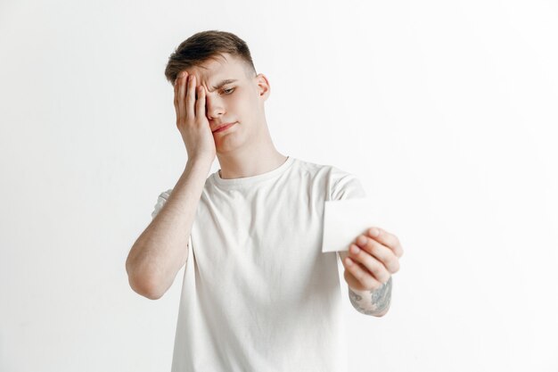 Jovem rapaz com um deslize de aposta de expressão de fracasso infeliz surpreso no fundo do estúdio. Emoções faciais humanas e conceito de apostas.