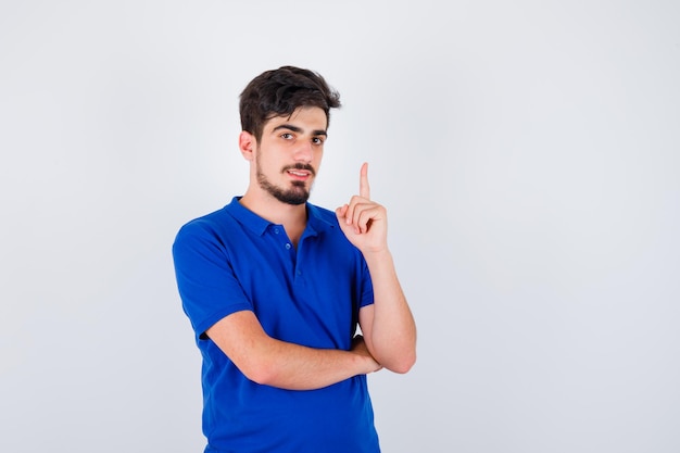 Jovem rapaz de t-shirt azul, levantando o dedo indicador em gesto de eureka e parecendo sensato, vista frontal.