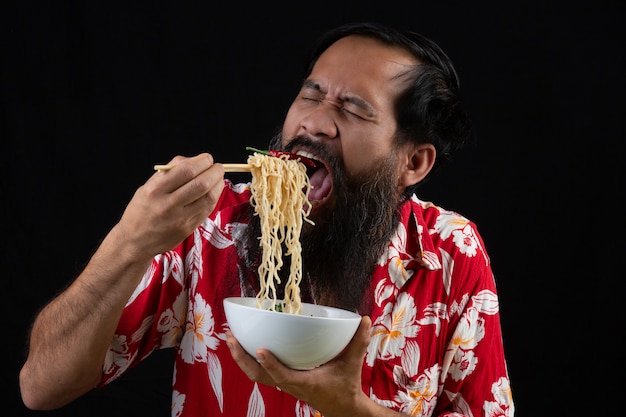 Jovem rapaz é desfrutar de comer macarrão instantâneo em casa.