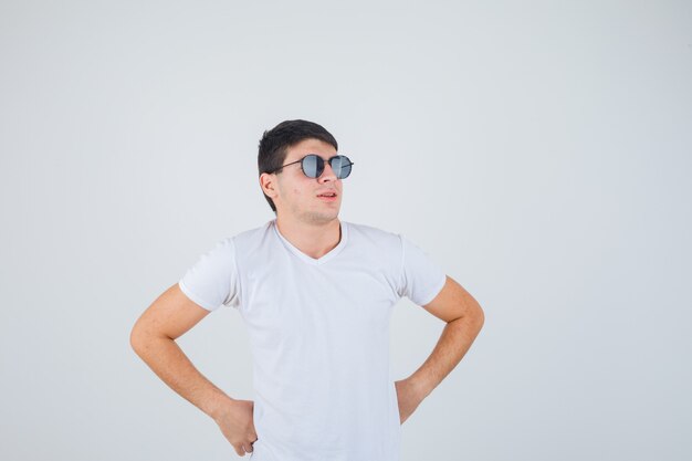 Jovem rapaz posando com as mãos na cintura em uma camiseta e parecendo autoconfiante. vista frontal.