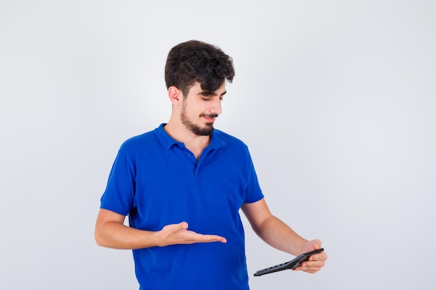 Jovem rapaz segurando calculadora e apontando para ela em t-shirt azul e parecendo feliz. vista frontal.