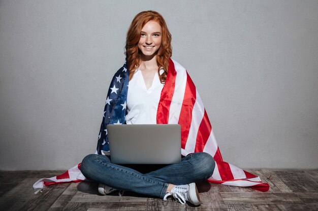 Jovem ruiva com bandeira EUA usando computador portátil