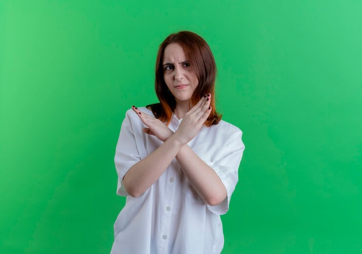 Foto grátis jovem ruiva descontente mostrando gesto de não isolado na parede verde