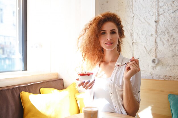 Jovem ruiva incrível sentado no café enquanto come a sobremesa.