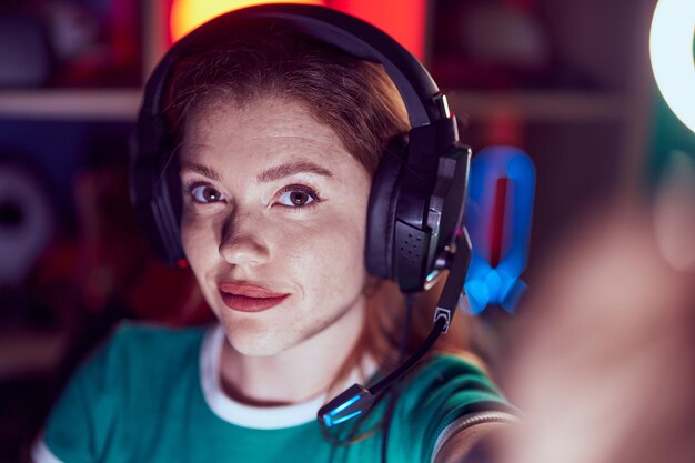 Jovem ruiva streamer sorrindo confiante fazendo selfie pela câmera na sala de jogos