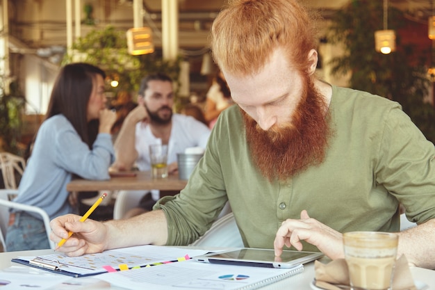 Jovem ruivo usando tablet em um café