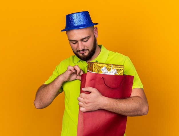 Jovem satisfeito com um chapéu de festa segurando e olhando para uma sacola de presente