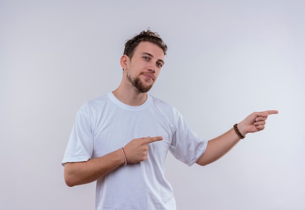 Jovem satisfeito vestindo uma camiseta branca apontando para o lado em um fundo branco isolado