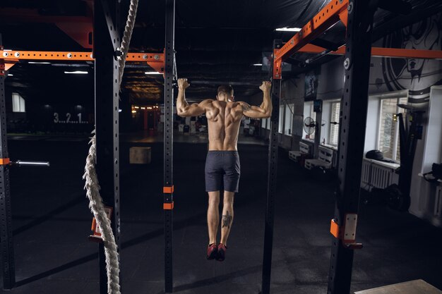 Jovem saudável, atleta fazendo exercícios, flexões no ginásio. Único modelo caucasiano praticando duro, treinando a parte superior do corpo. Conceito de estilo de vida saudável, esporte, fitness, musculação, bem-estar.