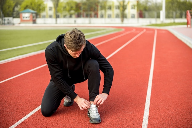 Foto grátis jovem saudável, sentado na pista de corrida, amarrando o cadarço