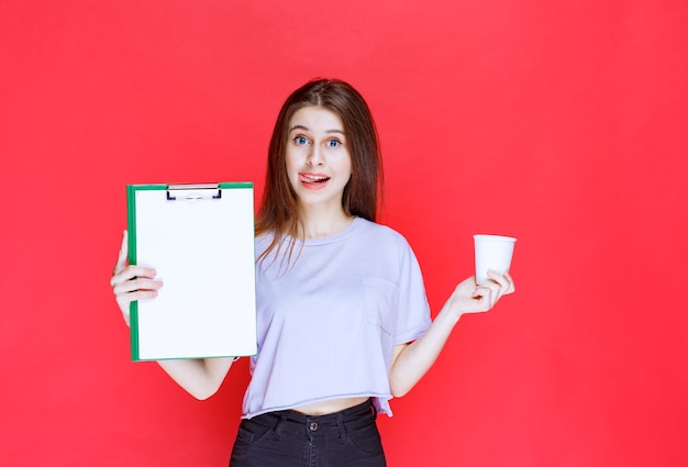 jovem segurando a folha de relatório e um copo de bebida.