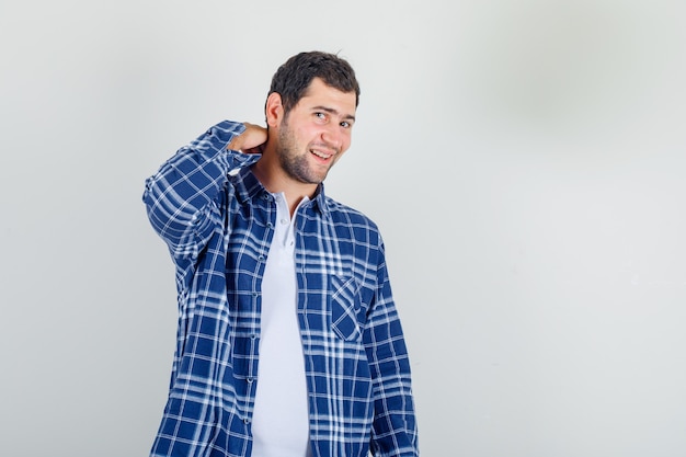 jovem segurando a mão em seu pescoço na camisa e parecendo alegre.