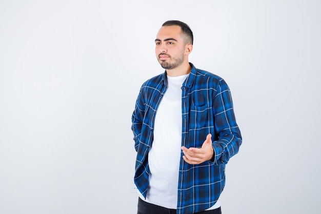 Jovem segurando a mão na cintura enquanto estica a mão segurando algo em uma camisa quadriculada e camiseta branca e parece feliz