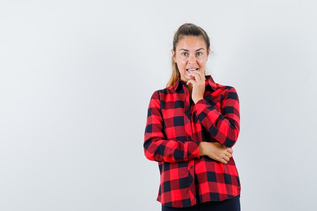 Jovem segurando a mão no queixo com uma camisa xadrez e parecendo sonhadora