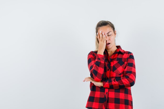 Jovem segurando a mão no rosto com uma camisa xadrez e parecendo com sono