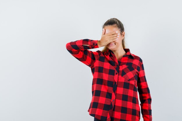 Jovem segurando a mão nos olhos com uma camisa quadriculada e parecendo feliz