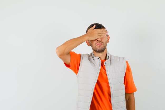 Foto grátis jovem, segurando a mão nos olhos em uma camiseta, jaqueta e parecendo quieto. vista frontal.