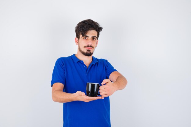 Jovem segurando a xícara com uma camiseta azul e olhando sério