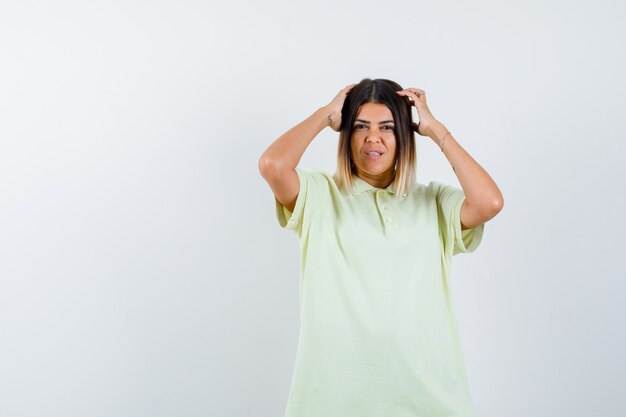 Jovem, segurando as mãos na cabeça em t-shirt e olhando desconfortável, vista frontal.