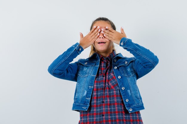 Jovem, segurando as mãos nos olhos na camisa, jaqueta e parecendo feliz. vista frontal.