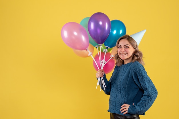 Jovem segurando balões coloridos e sorrindo em amarelo