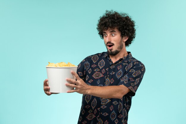 Jovem segurando batatas fritas em uma parede azul claro cinema masculino cinema filme cinema