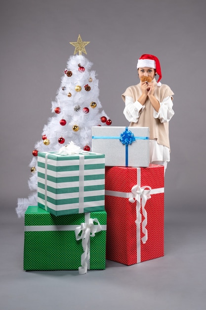 jovem segurando biscoitos no chão cinza perto da árvore de Natal e presentes