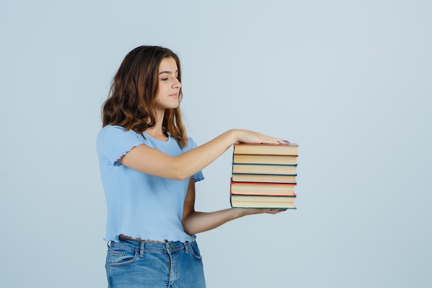 Jovem segurando livros em t-shirt, jeans e olhando com cuidado. vista frontal.