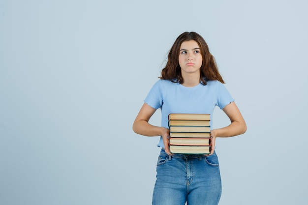 Jovem segurando livros em t-shirt, jeans e parecendo insatisfeita. vista frontal.