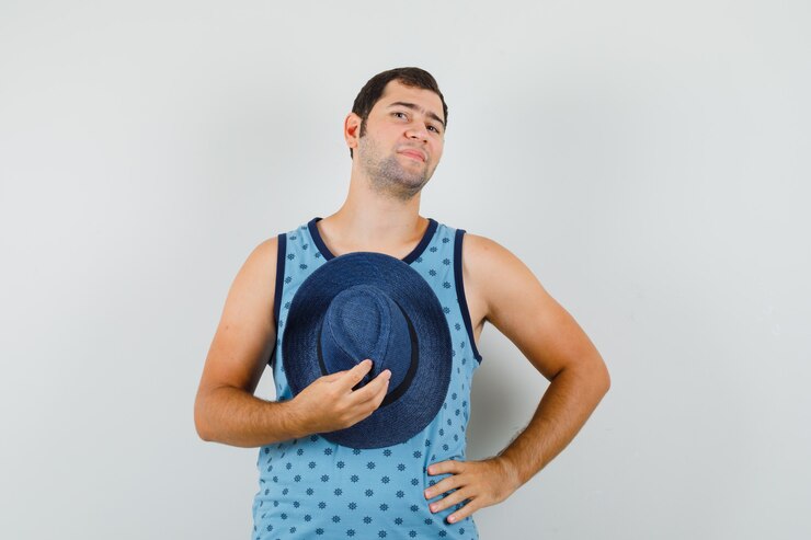 Foto grátis jovem, segurando o chapéu na camiseta azul e parecendo confiante.