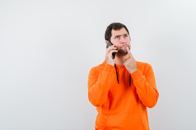 Jovem segurando o dedo na boca e ligando para alguém com o telefone no fundo branco