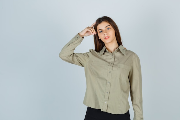 Jovem, segurando o dedo na cabeça na camisa, saia e olhando pensativa, vista frontal.