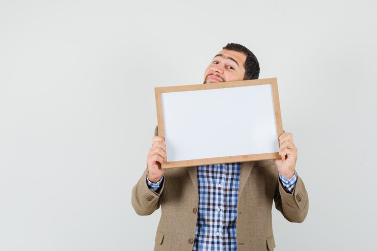 Foto grátis jovem, segurando o quadro em branco na camisa, jaqueta e olhando alegre, vista frontal.