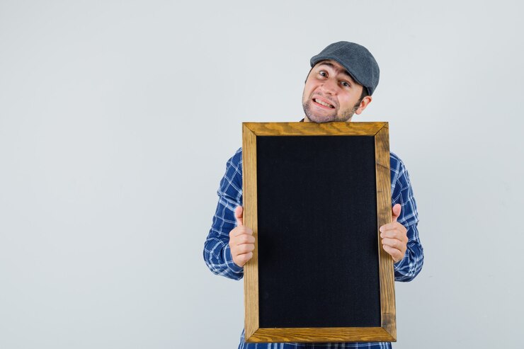 Foto grátis jovem, segurando o quadro-negro na camisa, boné e olhando bonito, vista frontal.