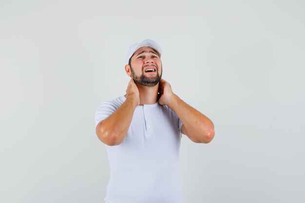 Jovem segurando seu pescoço em t-shirt, boné e parecendo deprimido. vista frontal.