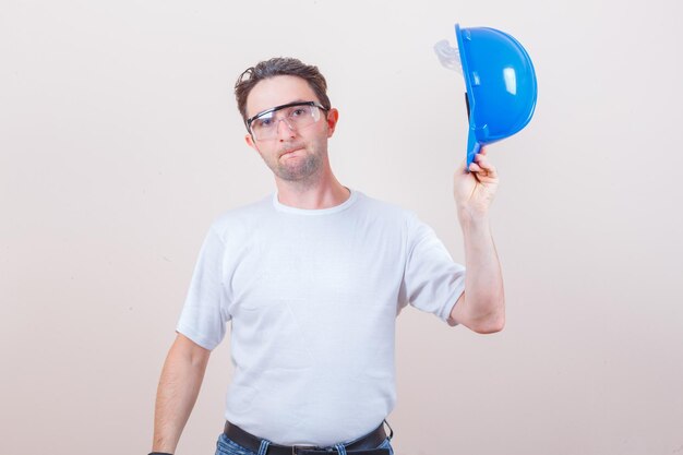 Jovem segurando um capacete em uma camiseta, jeans e parecendo confiante