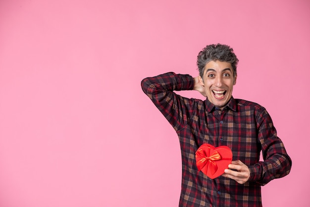 Jovem segurando um coração vermelho em forma de presente na parede rosa