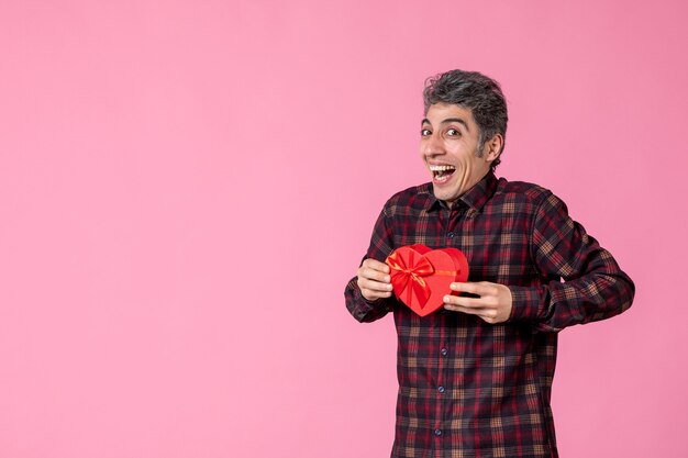 Foto grátis jovem segurando um coração vermelho em forma de presente na parede rosa