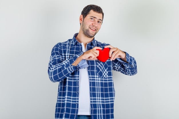 Jovem, segurando um coração vermelho na camisa e parecendo alegre.