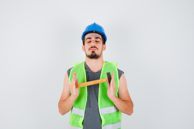 Jovem segurando um machado com as duas mãos e fechando os olhos em uniforme de construção e parecendo calmo