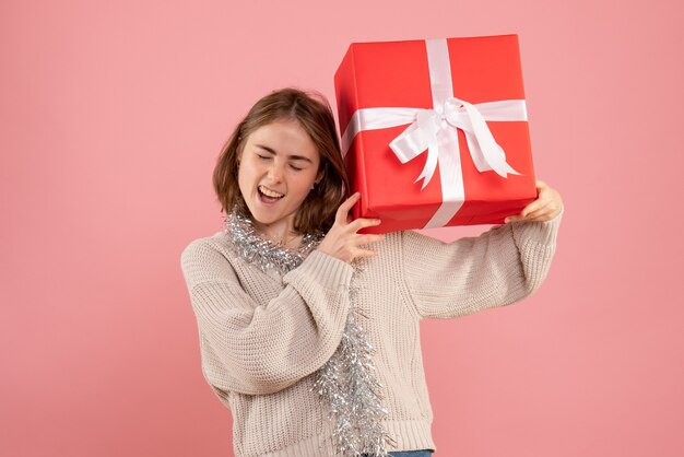 jovem segurando um presente de natal se sentindo animada na rosa