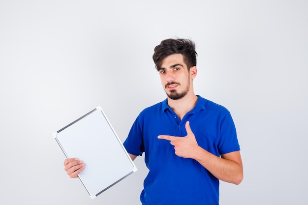 Jovem segurando um quadro branco com uma camiseta azul, apontando para ele e parecendo sério