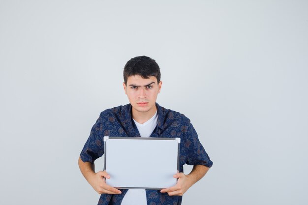 Jovem segurando um quadro branco em uma camiseta branca e uma camisa floral