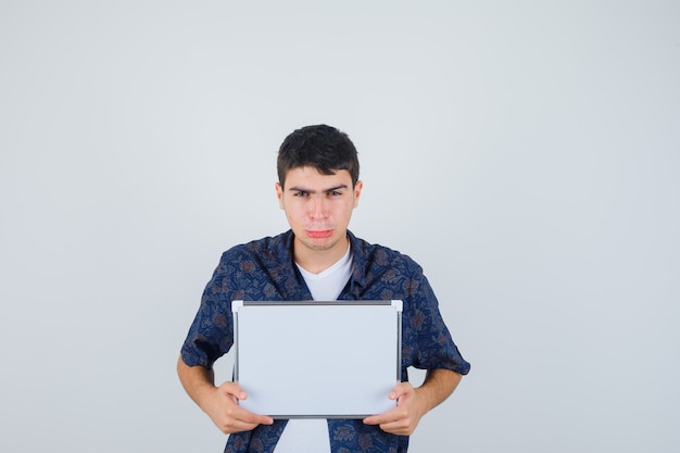 Jovem segurando um quadro branco, lábios curvos em uma camiseta branca e uma camisa floral