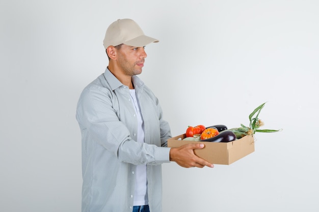 Jovem segurando uma caixa com legumes na camisa e no boné