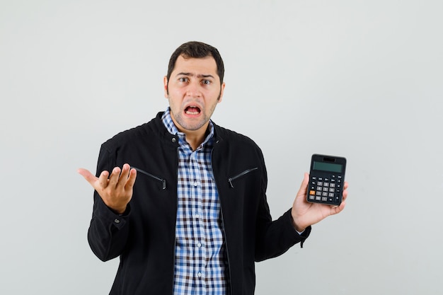 Jovem segurando uma calculadora com uma camisa, jaqueta e parecendo confuso